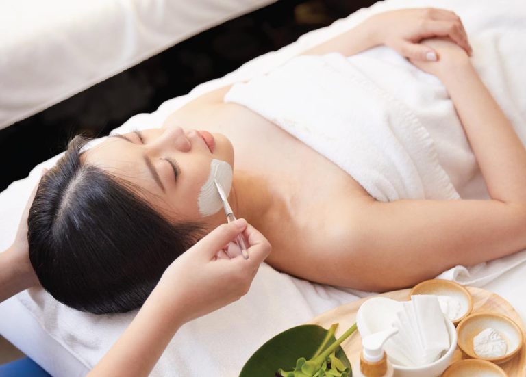 Hands Of Spa Therapist Applies Facial Product To A Woman Laying On Massage Table Bangkok Spa Siam SQ1